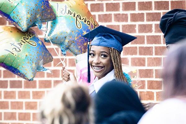 Adult High School graduate at graduation holding balloons 